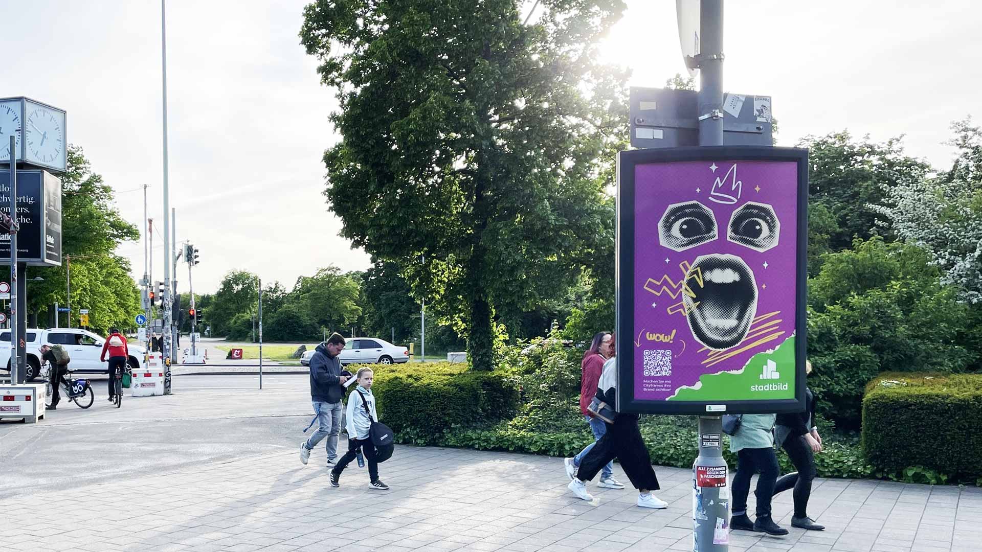 Werbeplakat mit einem großen Gesicht und bunten grafischen Elementen in einem städtischen Umfeld.