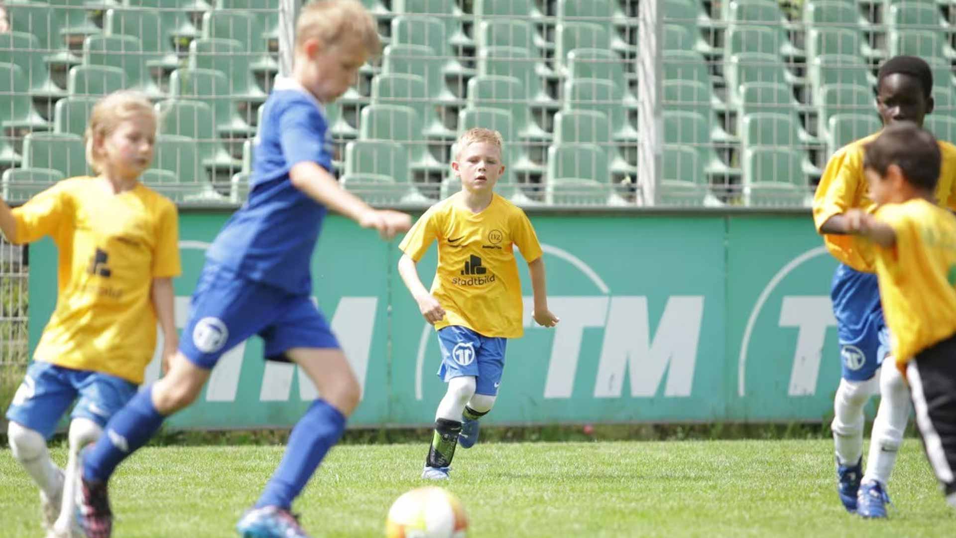 Gruppe von Kindern in gelben und blauen Trikots, die auf einem Fußballplatz spielen.