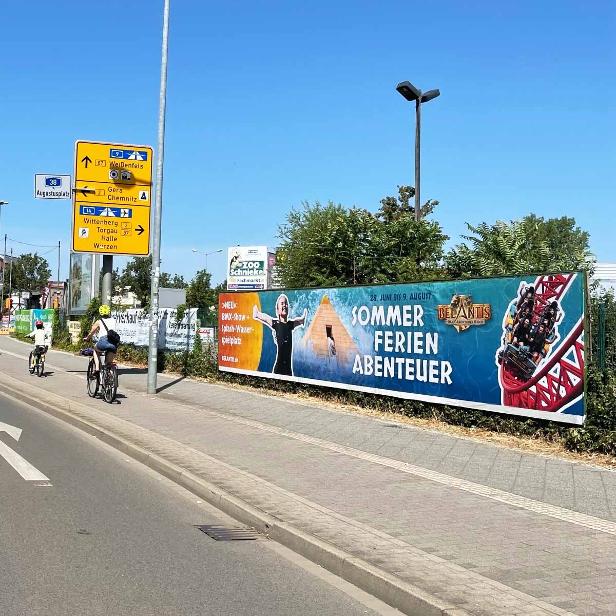 Ein großes Werbebanner, das für Sommerferienabenteuer wirbt, mit einer Achterbahn und einer Person, die die Arme hebt.