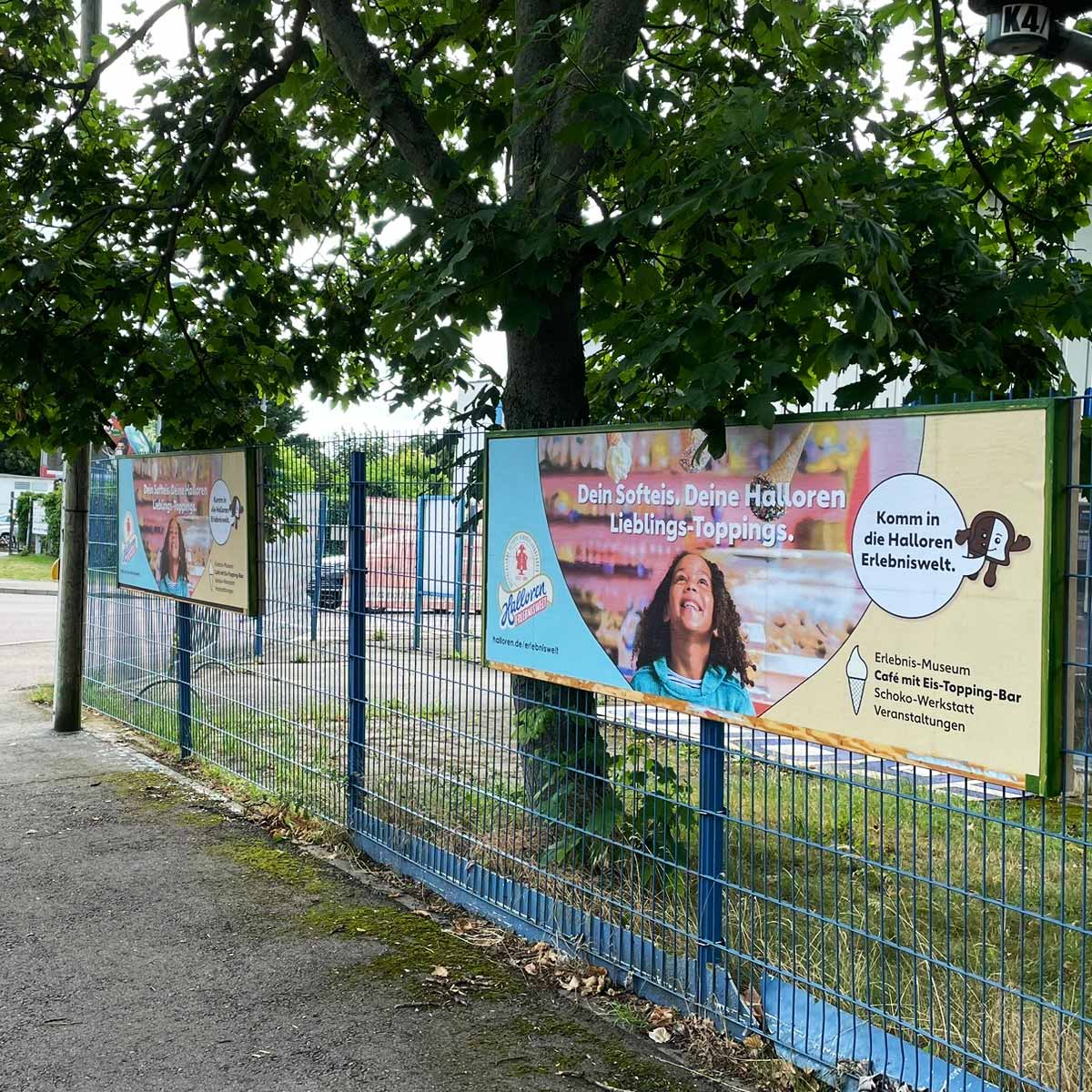 Zwei Werbebanner an einem Zaun, die verschiedene Eistoppings und ein Erlebnisangebot bewerben.