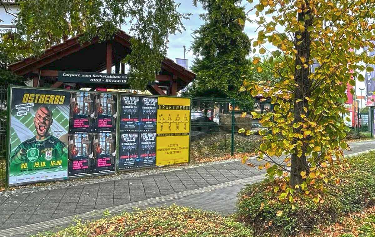 Plakatwand mit mehreren Ankündigungen für Veranstaltungen und einem Baum im Vordergrund.