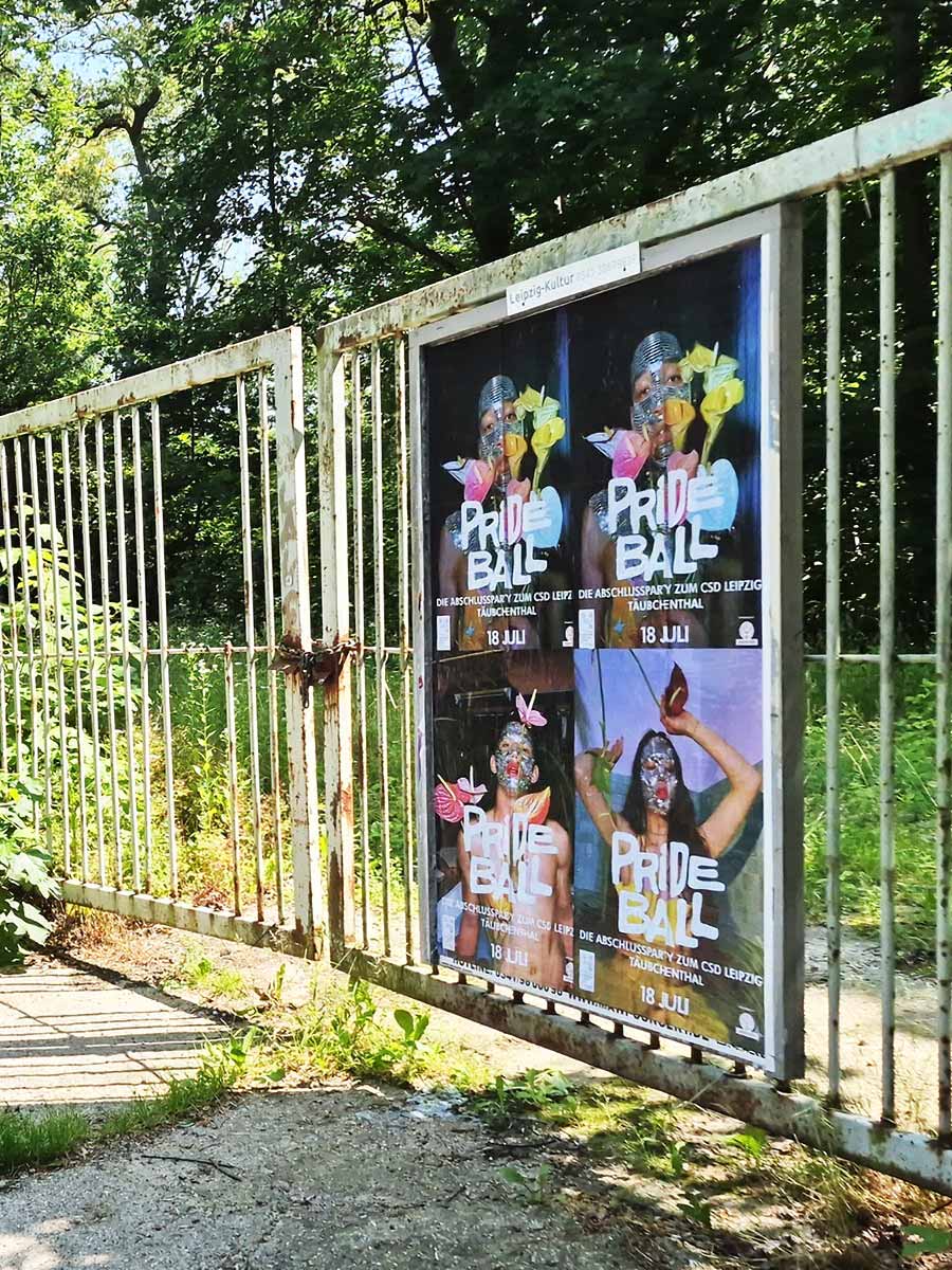 Hinter einem verwitterten Metallzaun hängen vier Prideball-Plakate mit dem Datum 18. Juli im grünen Leipziger Umfeld.